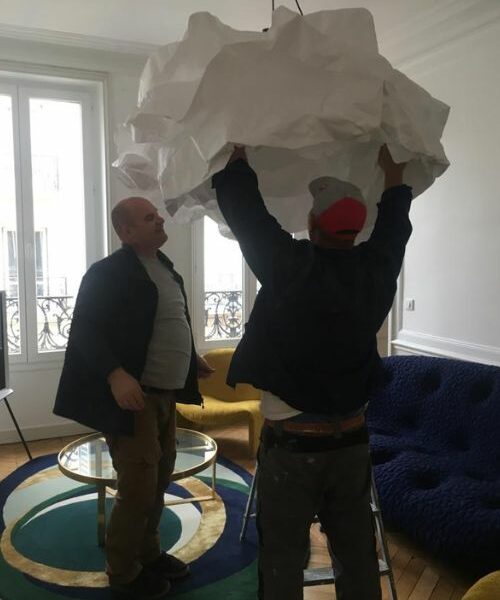 Deux hommes installant une suspension sculpturale dans un salon rénové