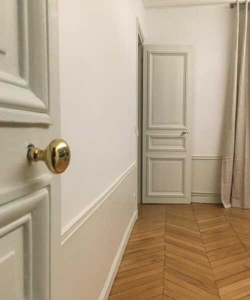 Vue intérieure d’un couloir avec moulures, parquet et poignées dorées