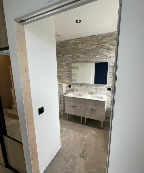 salle de bain rénovée avec mur en pierre et meuble double vasque à Paris